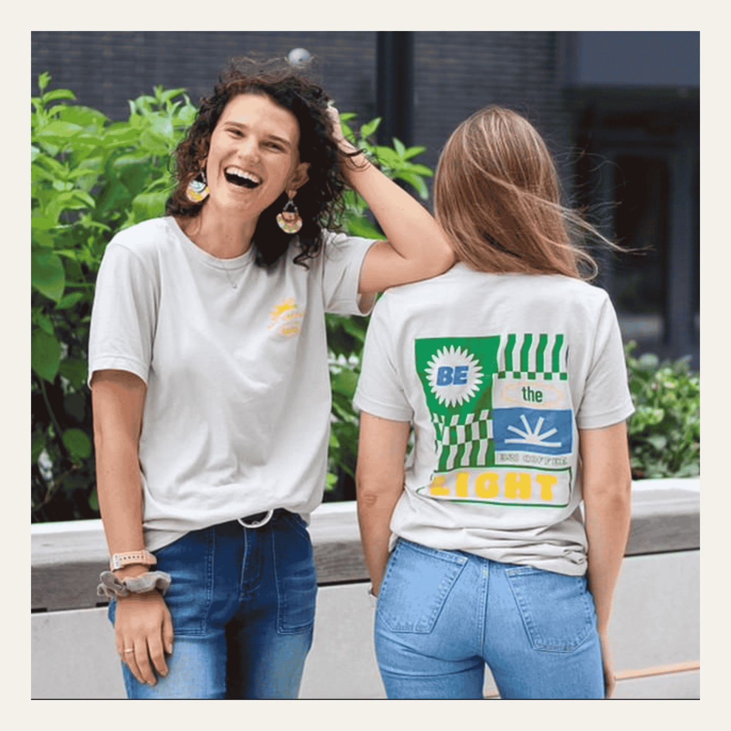 Two women wearing tan t-shirts with colorful designs outdoors.