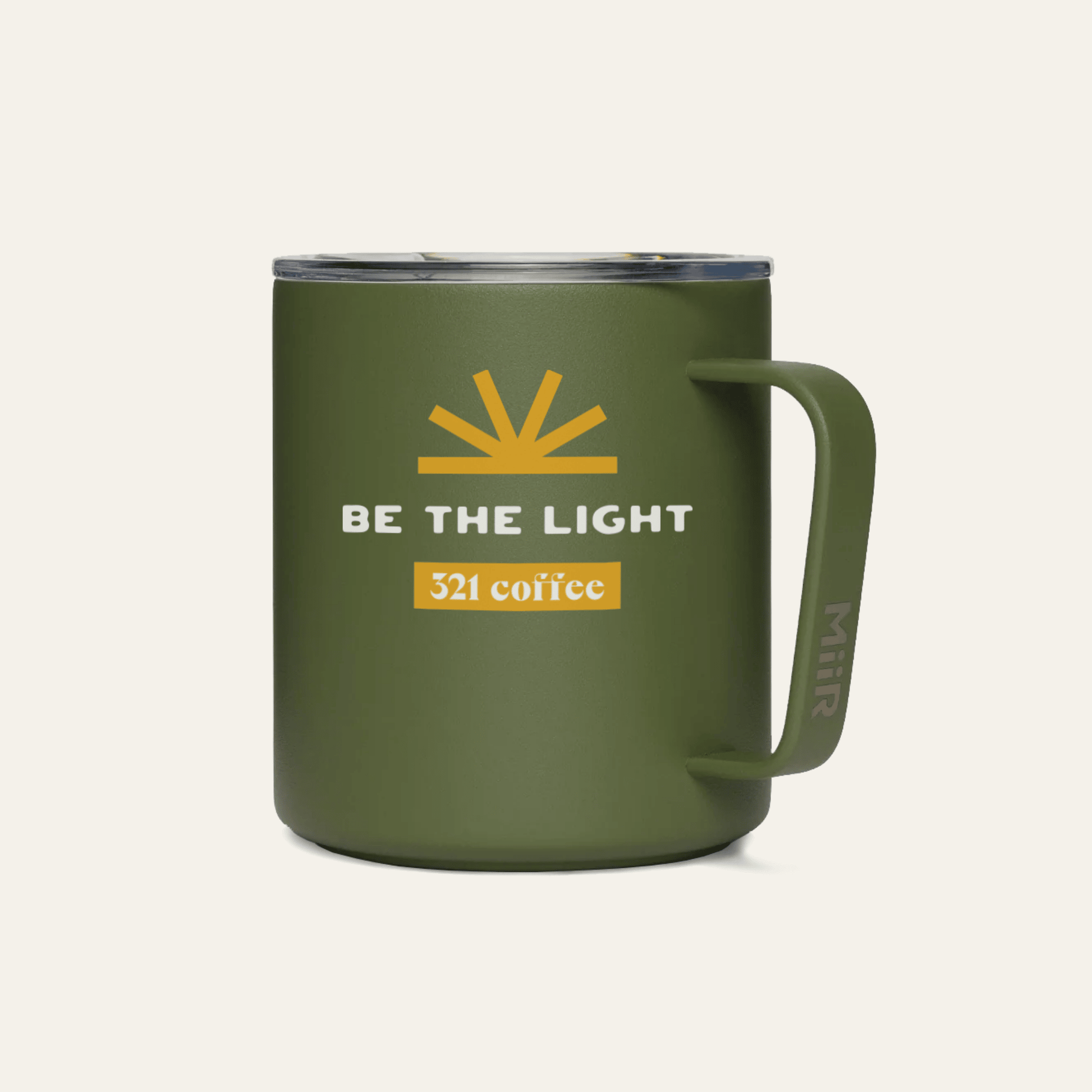 A dark green metal camp mug with "Be the Light" printed in white on the mug with a yellow sun above it.