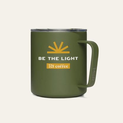 A dark green metal camp mug with "Be the Light" printed in white on the mug with a yellow sun above it.
