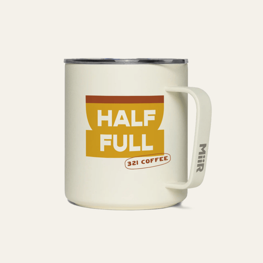 A light beige metal camp mug with "Half Full" printed in white on a yellow coffee mug.