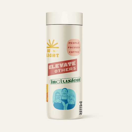 The back side view of 321 Coffee's tumbler. The tumbler is beige and contains elements of 321 Coffee branding, such as sayings like "Rise Up" and "Love Big". The branding is very colorful.